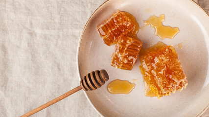 Flatlay honey in honeycomb on a plate with a wooden honey spoon on a linen tablecloth. Copy space.