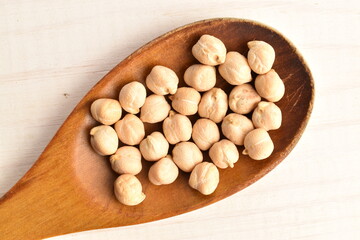 Uncooked hummus grains, close-up, on a white wooden table.