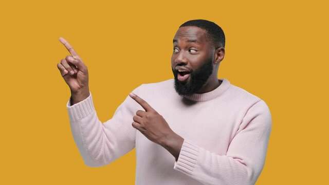 Close up portrait of a happy young man pointing finger showing copy space on yellow background