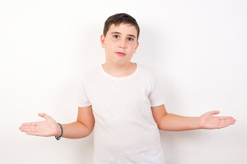 Maybe yes or no. Doubtful Caucasian young boy standing against white background  shrugs shoulders in bewilderment, tries to make decision puzzled what he wants. Hesitation and uncertainty.