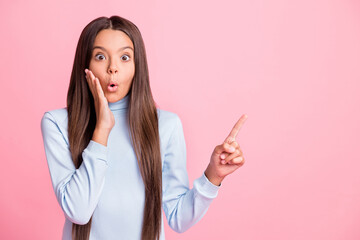 Portrait of school girl shocked hand on cheek indicate finger empty space isolated on pink color background