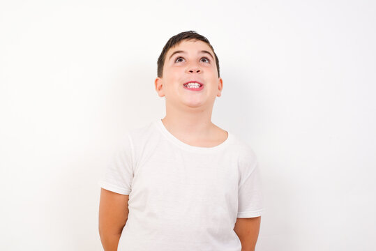 Portrait of mysterious Caucasian young boy standing against white background looking up with enigmatic smile. Advertisement concept.