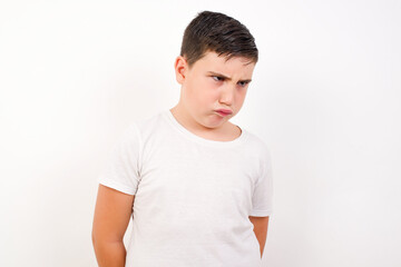 Caucasian young boy standing against white background with snobbish expression curving lips and raising eyebrows, looking with doubtful and skeptical expression, suspect and doubt.