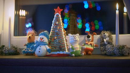 Cute atmospheric window sill decoration with handcrafted knitted toys and a gingerbread Christmas tree decorated with patterns of Christmas toys and a red star.