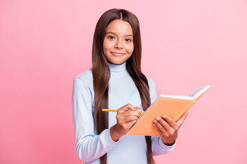 Portrait of attractive cheery content brainy girl writing notes copybook diary isolated over pink pastel color background