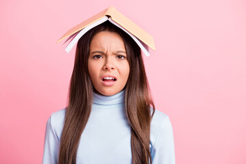 Close-up portrait of attractive displeased bored tired girl wearing book on head isolated over pink...