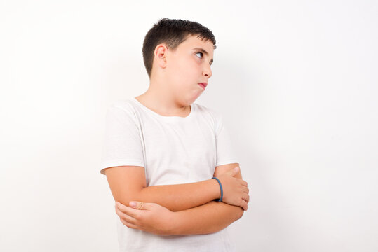 Image of upset Caucasian young boy standing against white background  with arms crossed. Looking with disappointed expression aside after listening to bad news.