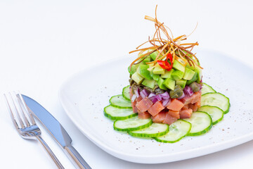 Trout tartare (tartar) with avocado, cucumber, capers and red onion. Decorate with fried leeks and chili peppers. Close-up, white background.