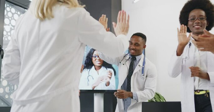 Attractive experienced positive successful diverse medical people greeting each other with high five after right get decision during video conference with female colleague