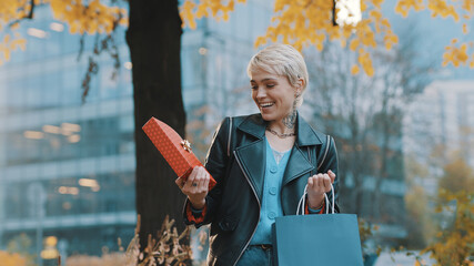 Happy caucasian woman in leather jacket taking out the present from the bag with surprised and satisfied laugh. High quality photo