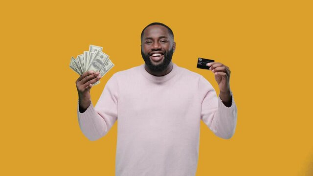 black man shows cash or credit card. money banknotes and card, african american man guy with success in cash financial freedom on yellow background