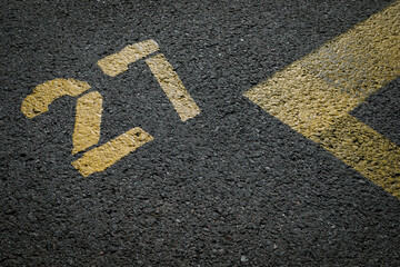 sign on the asphalt, yellow painted number twenty seven on grey street, yellow lines like a corner on the road, 
space for text 