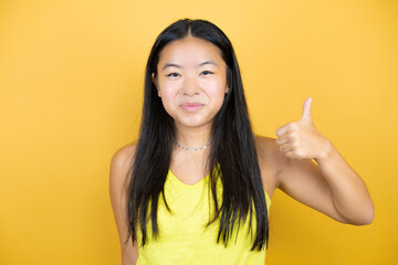 Young beautiful asian woman over yellow isolated background smiling and doing the ok signal with her thumb