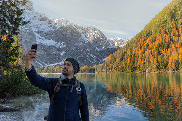 A man is taking a photo with a lake and mountains in the background.