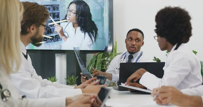 Attractive confident experienced successful diverse medical team which holding a meeting in boardroom and consulting as to the results of x-ray of patient with female colleague via video call