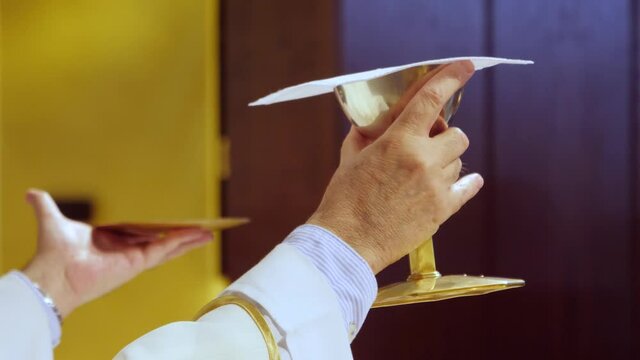 hand of a priest raising the holy chalice that represents the blood of christ and the sacred form that represents the body of christ during the office of holy mass