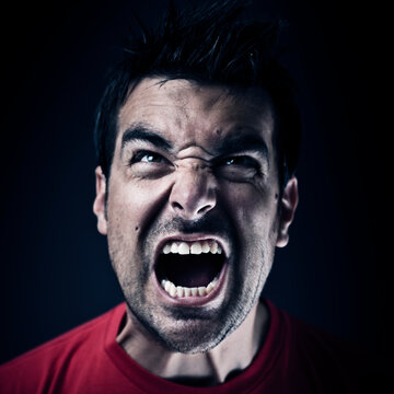 Dark short haired man in red t shirt  screaming of pain and anger. Studio photo, dark setting.