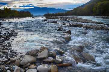 Beautiful landscape with high mountains with illuminated peaks, stones in mountain lake, reflection, blue sky and sunrise. HDR