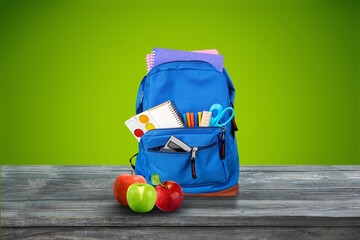 Classic school backpack with colorful school supplies and books on desk.