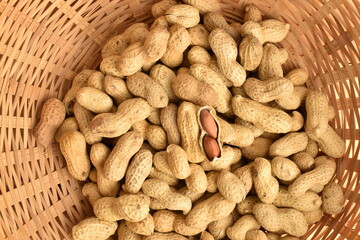 Unshelled organic peanuts, close-up, in a straw bowl.