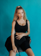 Sweet blonde sitting on a bar stool in the studio. Turquoise background.