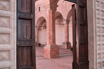 The entrance of a medieval abbey with a wooden door, brick columns and arches (Gubbio, Umbria, Italy)