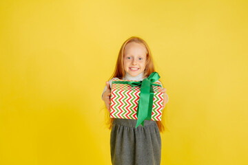 Giving and getting presents on Christmas holidays. Teen smiling girl having fun, holding big gifts isolated on yellow studio background. New Year 2021 meeting, childhood, happiness, emotions.