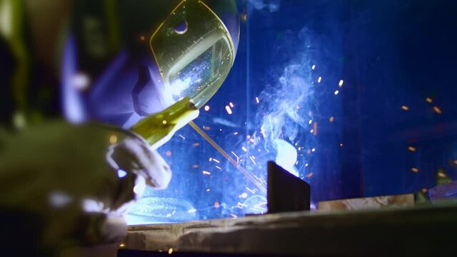 Factory worker welds metal. The man is welding. Welding with argon or electrode, using a welding machine. An industrial enterprise producing metal structures. Sparks and flashes fly. Slow motion