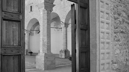Obraz na płótnie Canvas The entrance of a medieval abbey with a wooden door, brick columns and arches (Gubbio, Umbria, Italy)