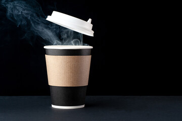 Black cup of coffee with a white cap on a black background. Hot drink with steam.