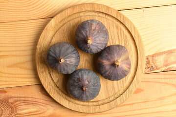 Ripe dark blue organic figs on a wooden round tray, close-up, on a wooden table.