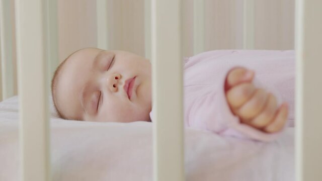 Cute little baby sleeps sweetly in his crib and sees colorful dreams in bedroom while sleeping.