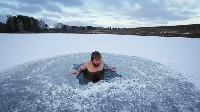 Winter swim. Young man with beard swims in a winter lake. Scene 1, camera 1