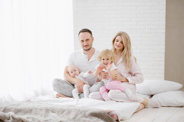A young Caucasian family with two children daughters in a white home interior. Home clothes.