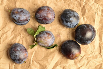 Ripe dark blue organic plums, close-up, on brown paper.