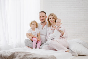 A young Caucasian family with two children daughters in a white home interior. Home clothes.