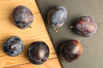 Ripe dark blue organic plums on a slate board and a wooden table, close-up.