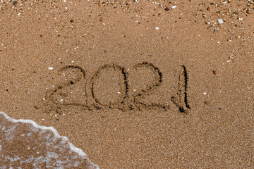 number 2021 is written on the sand at sea. waves and sand. 2021