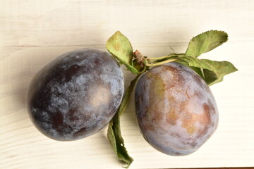 Ripe dark blue organic plums, close-up, on a white wooden table.
