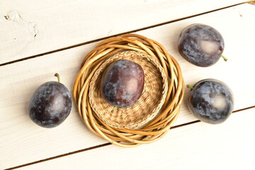 Ripe dark blue organic plums, close-up, on a white wooden table.