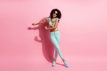 Full length body size photo of careless happy black skinned woman dancing on floor in casual outfit sunglass isolated on pastel pink color background