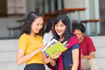Beautiful young asian woman reading book with classmates studying in background. University students studying together in class.