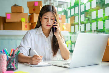 Starting a Small Business SME Owner Female Entrepreneur is talking on the phone with clients to receive And check orders online to prepare to pack boxes of goods for sale to customers, sme business id