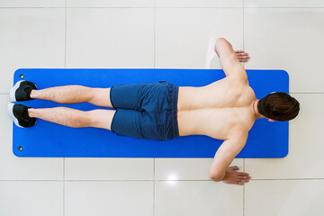 Top view handsome man doing push-up exercise on a blue exercise mat. Muscular and strong guy...