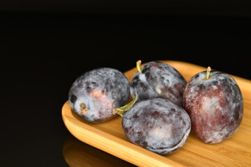 Ripe dark blue organic plums, close-up, on a black background.