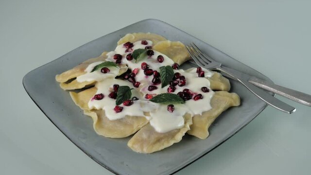 Fresh dumplings with fruit served on a plate decorated with nuts, pomegranate seeds in cream and chocolate glaze, Camera movement from the bottom up