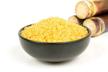 Sugar from sugarcane in black bowl and pile of sugarcane isolated on white background.