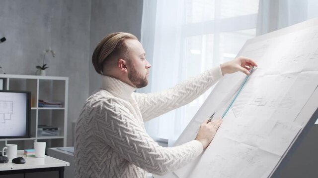 Concentrated architect works in loft using drawing board. Workplace of young engineer in modern office.