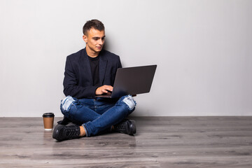 Young man working on laptop sitting on floor reading news, surfing net or freelancing isolated on...