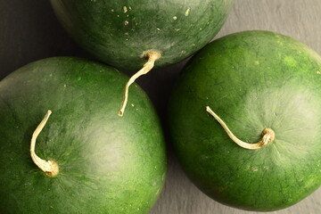 Three ripe organic watermelons, close-up, on a slate board.
